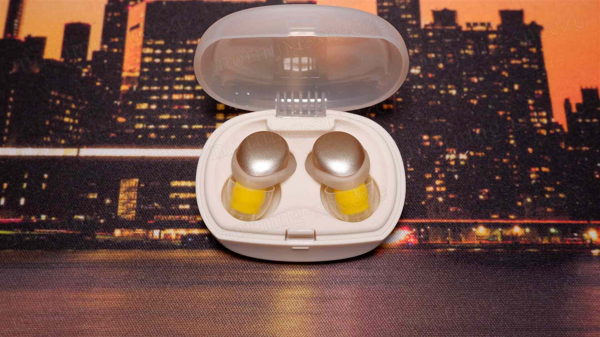 透明なケースに入った二つのイヤフォン。イヤフォンは金色の部分があり、ケースは白色。