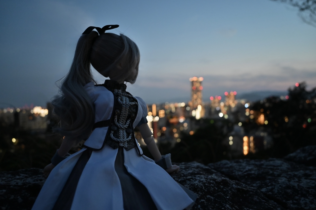 石垣から街を振り返るギンカ。顔は見えず、ポニーテールと体の輪郭がシルエットになって、日の沈みかけた街を背景に浮かんでいます。