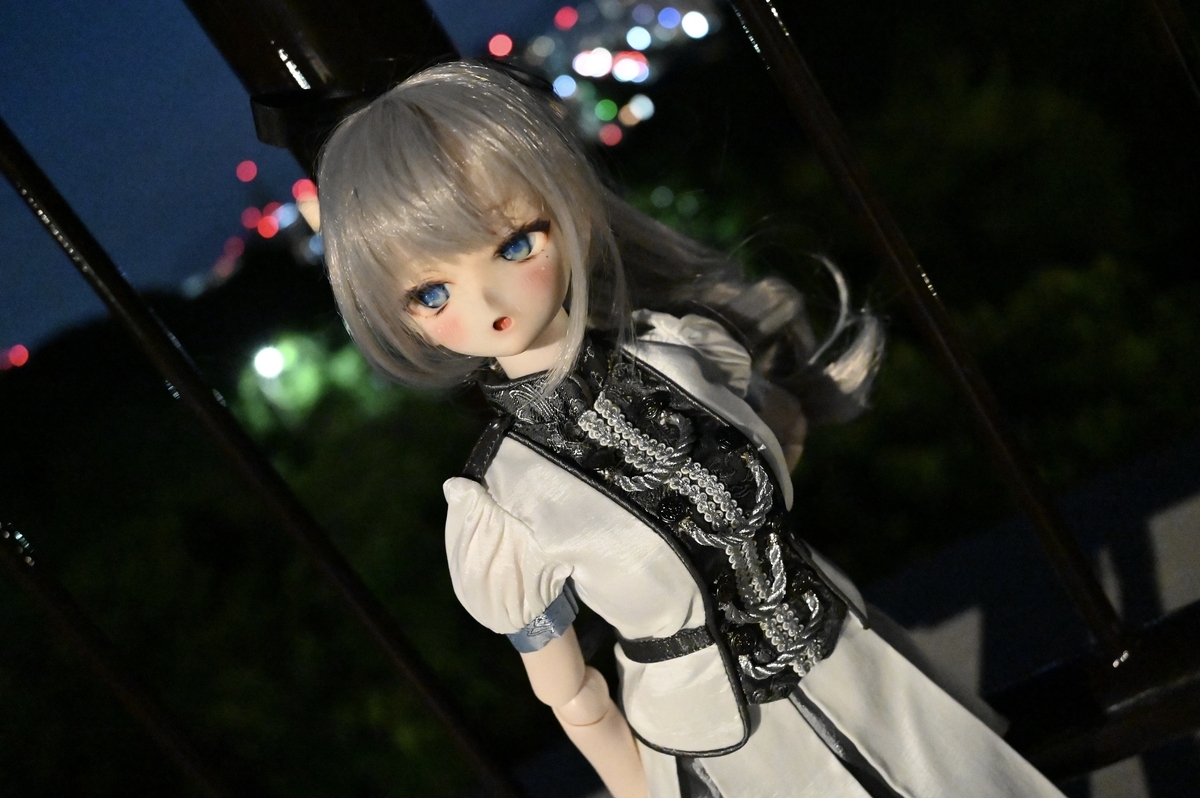 完全に日が沈んでいる写真。ギンカは夜景を背景に、左腕を後ろに回し鉄柵にもたれかかっています。