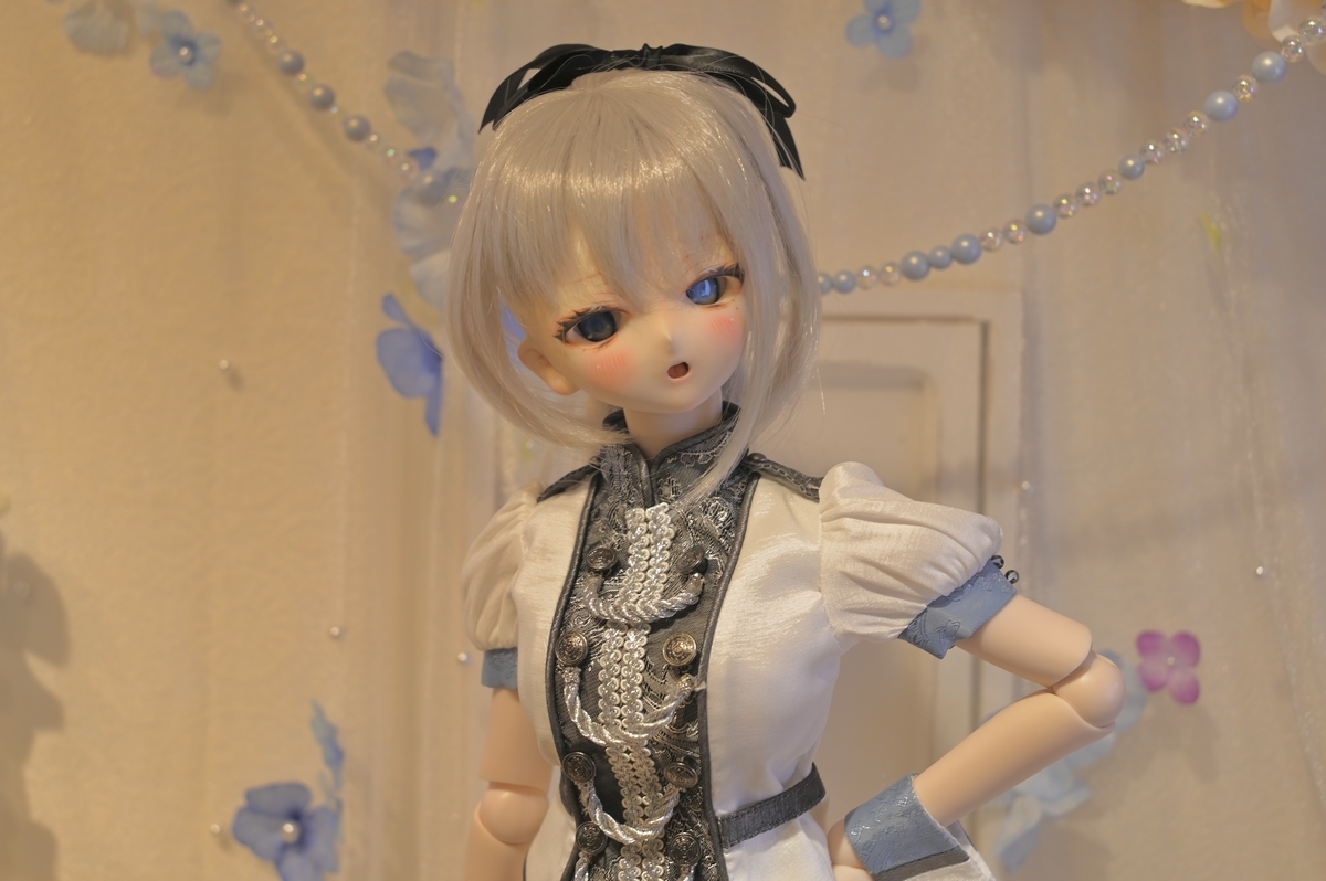 白い背景で、左拳を腰に当てているギンカ。左目は光を反射して淡く光っています。