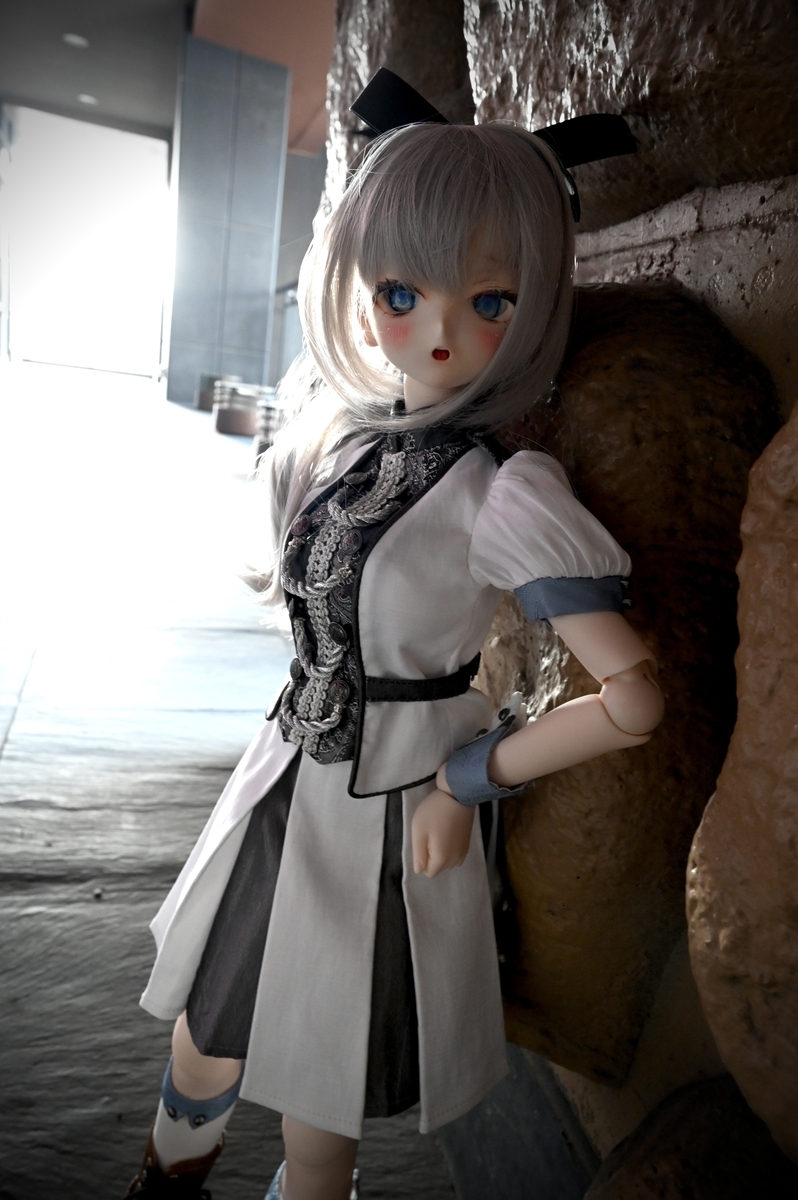 壁に寄りかかるギンカ。通路の奥は外の光が入り込み白飛びしています。