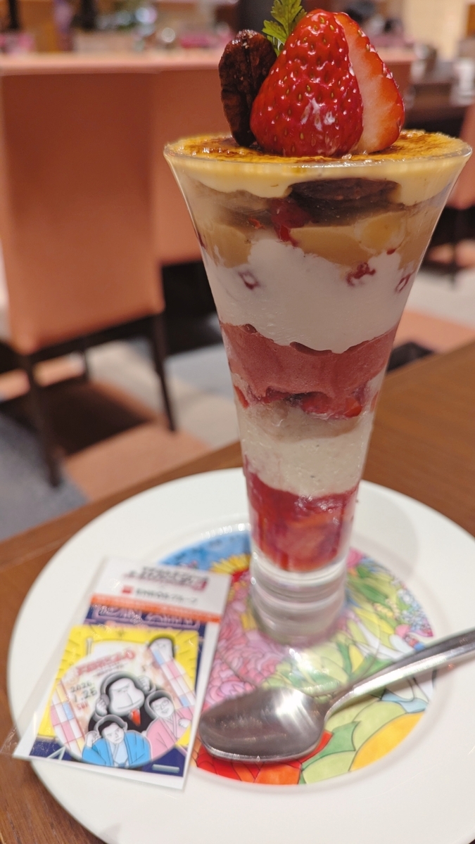苺が乗ったパフェ。パフェが乗った皿の上に、マヂカルラブリーとエネゴリくんのイラストのステッカーを乗せている。