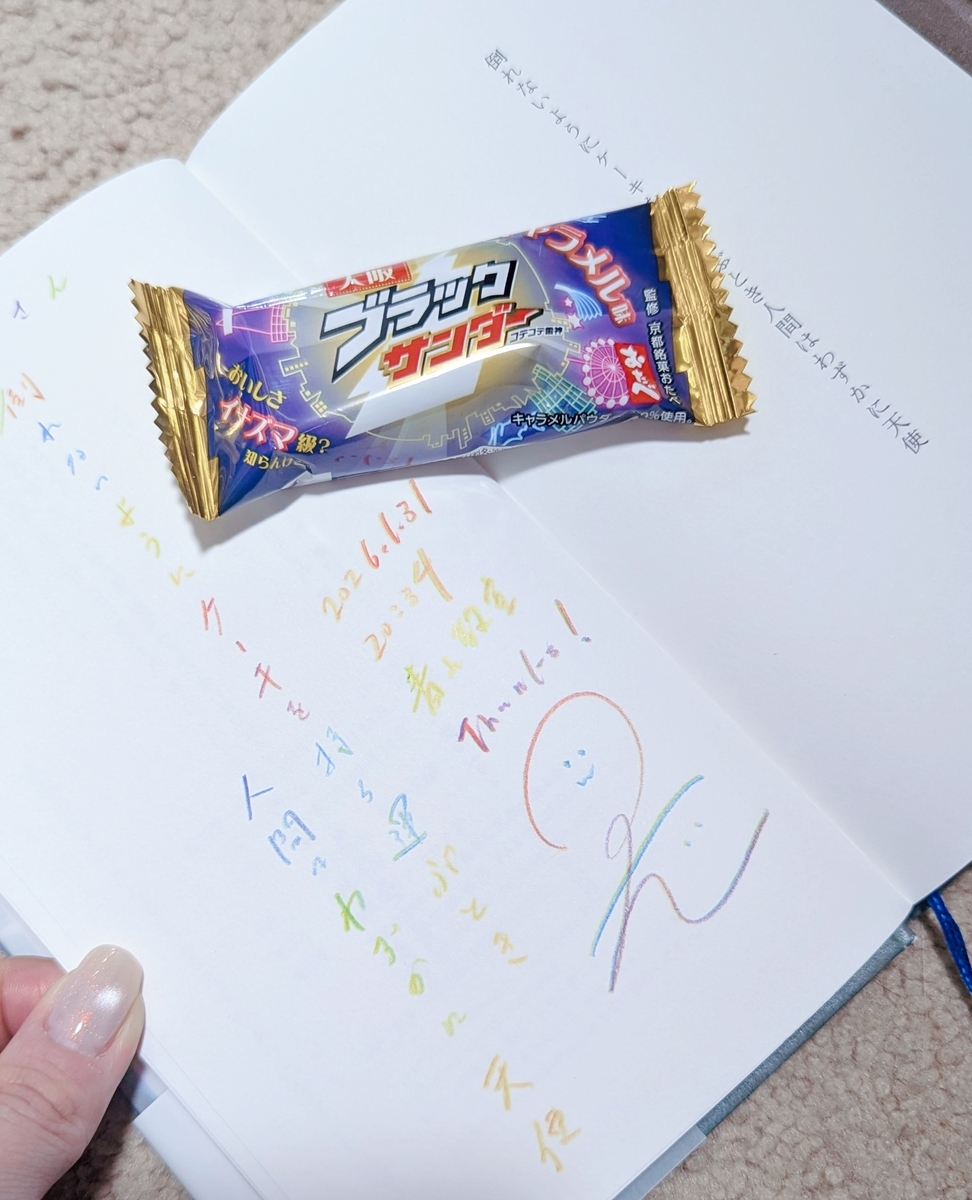 広げた本の上に大阪限定ブラックサンダーのキャラメル味が置かれている。本にはカラフルな文字で岡野大嗣のサインや日付、「倒れないようにケーキを持ち運ぶとき人間はわずかに天使」という短歌が書かれている。
