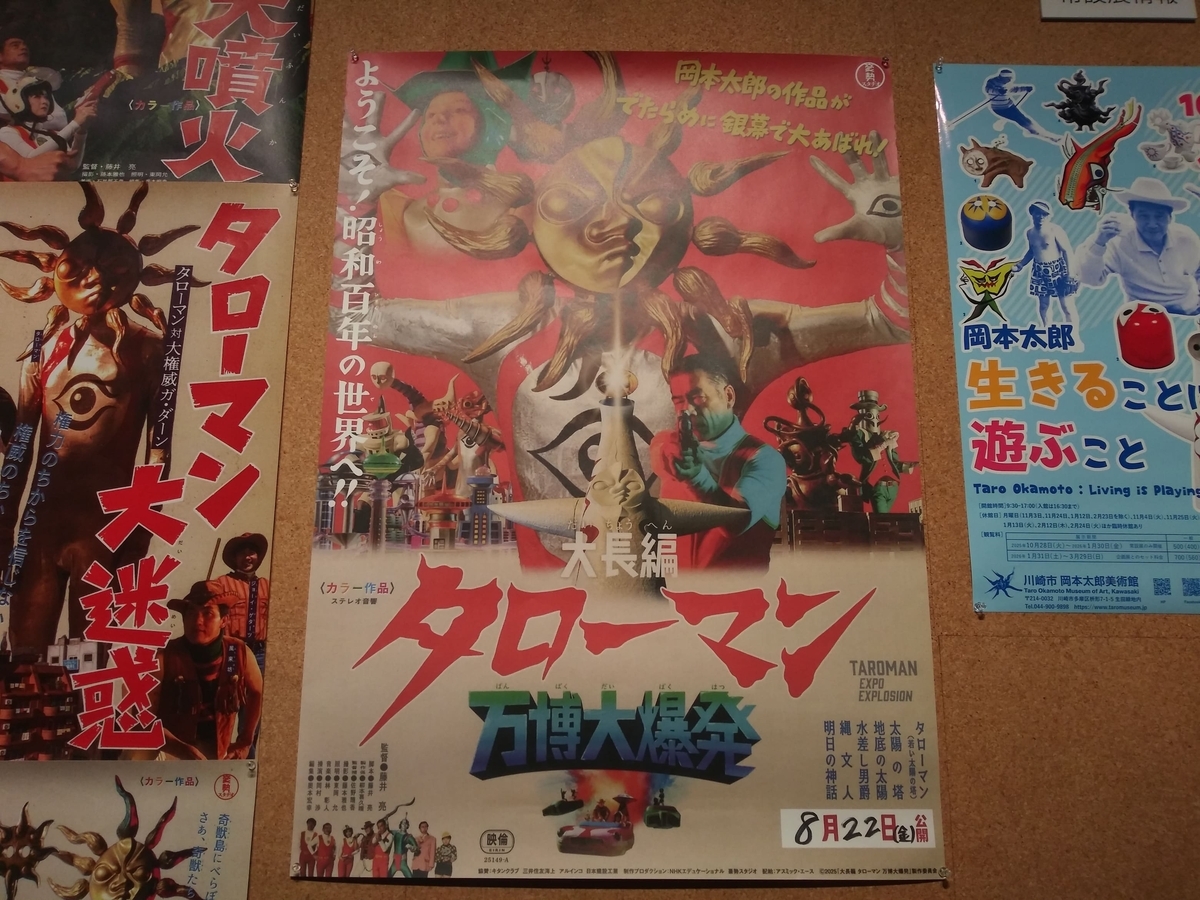 川崎市岡本太郎美術館「タローマン大万博川崎パビリオン」岡本太郎美術館情報の壁　常設展示のポスターの横に劇場版の「大長編　タローマン　万博大爆発」のポスターのアップ