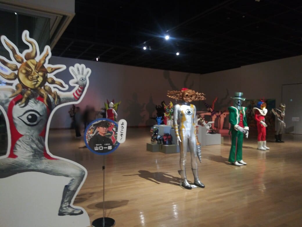 岡本太郎美術館　企画展示室「タローマン大万博川崎パビリオン」タローマンのパネルの隣に劇場版に登場した奇獣の人形がずらっと並んでいる様子