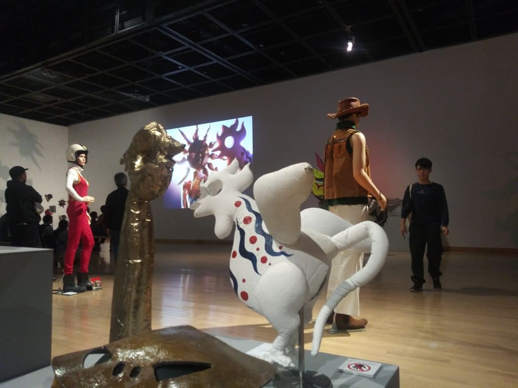 岡本太郎美術館　企画展示室「タローマン大万博川崎パビリオン」奇獣夢の鳥がタローマンに調理される映像を背景に奇獣夢の鳥と奇獣火の接吻が並んで映っている