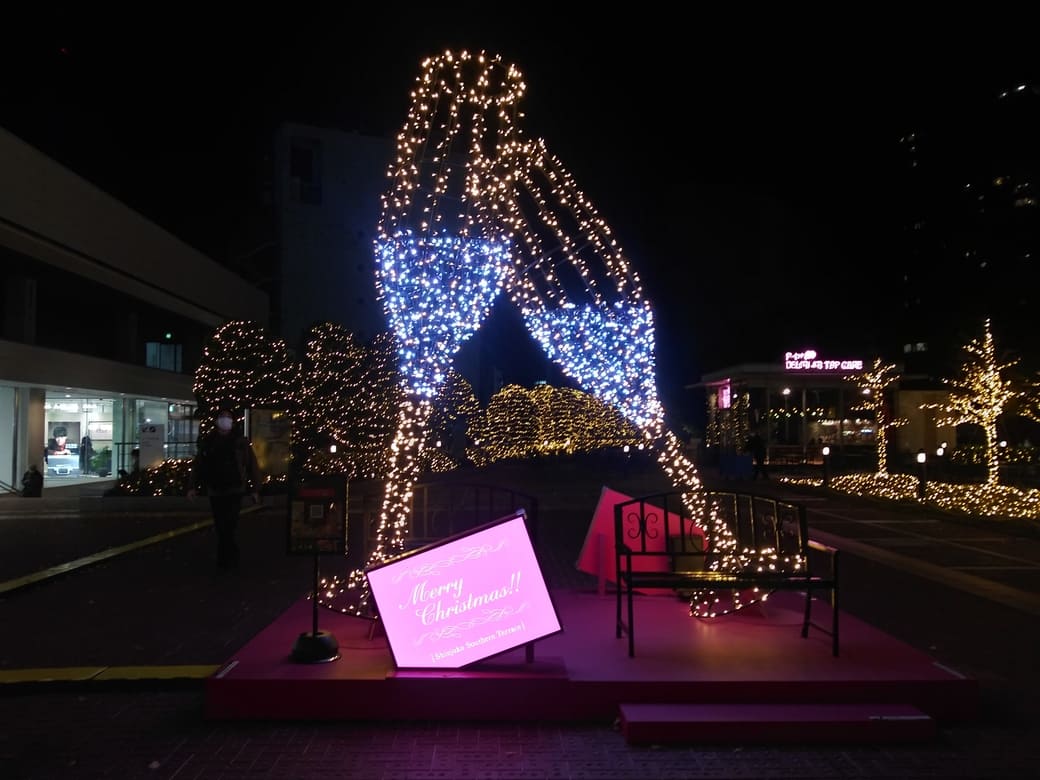 新宿南口_新宿サザンテラス_広場　大きなシャンパングラスのオブジェ　フルートシャンパングラスが還付委するように傾向きあっている、その下にmerryChristmasと書かれているピンク色のプレートが置いてある