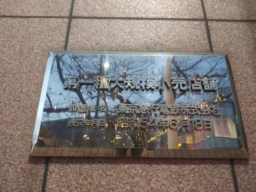 たまプラーザのクリスマスイルミネーション2025　ノースプラザ(東急百貨店たまプラーザ店)正面入口右にある大店法プレートにイルミネーションが反射している