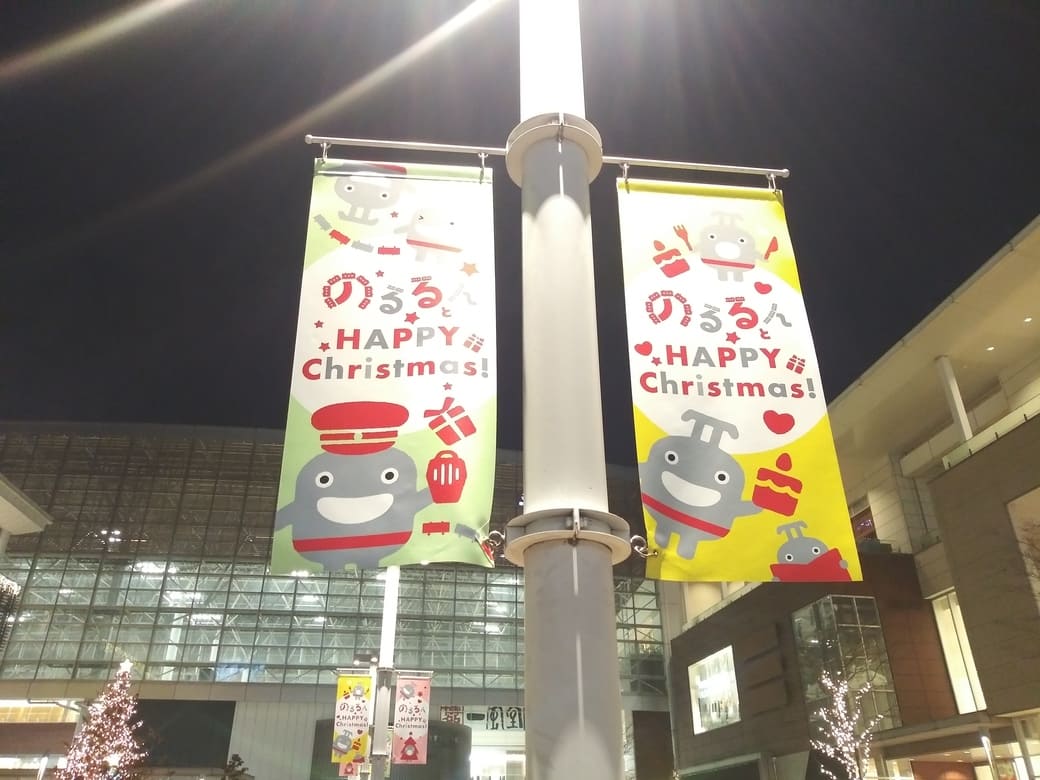 たまプラーザのクリスマスイルミネーション2025年_GATE PLAZA(ステーションコート_交番前)　横断歩道を渡って正面の照明に早くものるるんのバナーフラッグが出迎えてくれる　これは黄色と黄緑の2枚