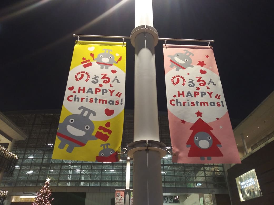 たまプラーザのクリスマスイルミネーション2025年_GATE PLAZA(ステーションコート_交番前)　横断歩道を渡って正面の照明に早くものるるんのバナーフラッグが出迎えてくれる　これは黄色とピンクの2枚
