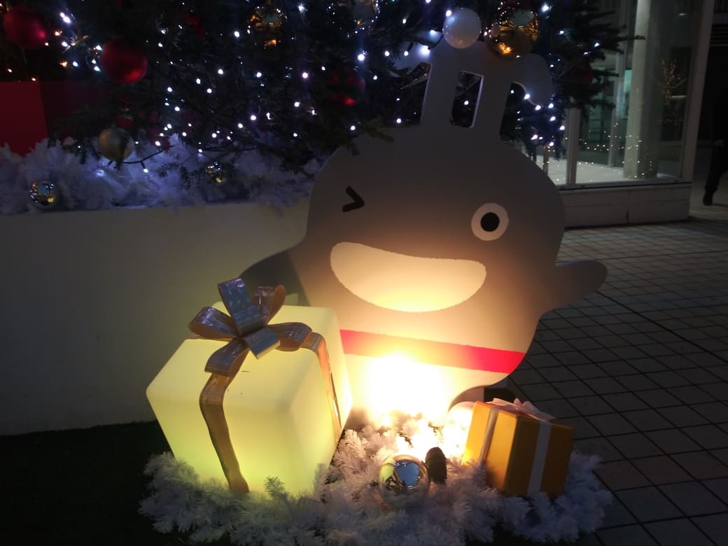たまプラーザのクリスマスイルミネーション2025年_GATE PLAZA_ステーションコート_駅前のクリスマスツリー　プレゼントを前にウインクするのるるん