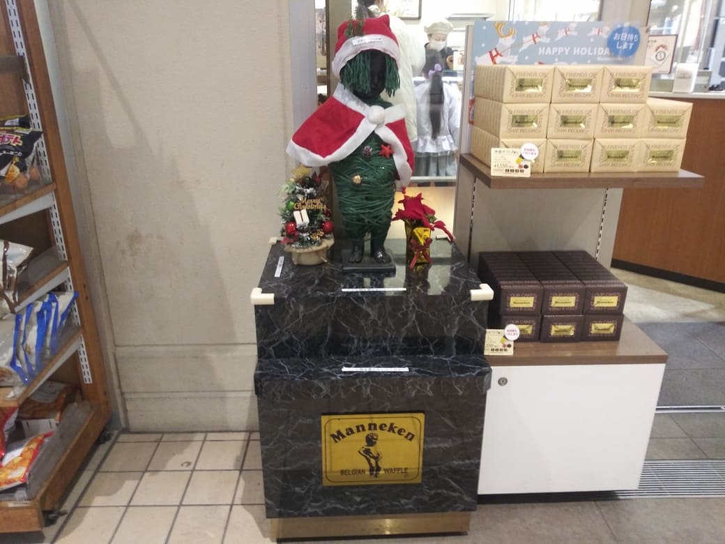 たまプラーザのクリスマスイルミネーション2025年_GATE PLAZA_ステーションコート_駅前マネケンがの銅像にサンタコスを着せている