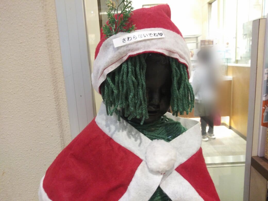 たまプラーザのクリスマスイルミネーション2025年_GATE PLAZA_ステーションコート_駅前　マネケンの銅像のアップ、垂れ下がった緑の毛糸は髪の毛を模しているように見えるが藻が貼り付いてるように見えて怖い