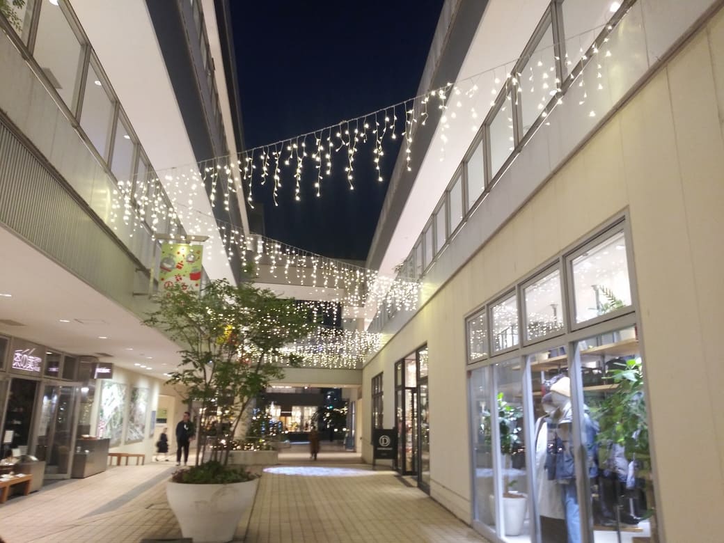 たまプラーザのクリスマスイルミネーション2025年_GATE PLAZA_カルディから交番までの通路中央のロゴスポットライトにものるるんが映っている