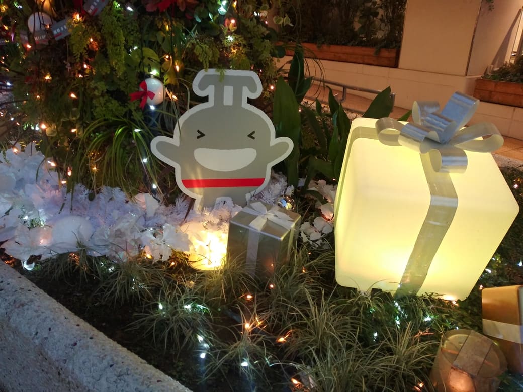 たまプラーザのクリスマスイルミネーション2025年_GATE PLAZA_交番側からカルディ方向への通路植え込みにあるのるるんのオブジェとライトアップされたディスプレイ　笑顔ののるるんと光るプレゼントの包み