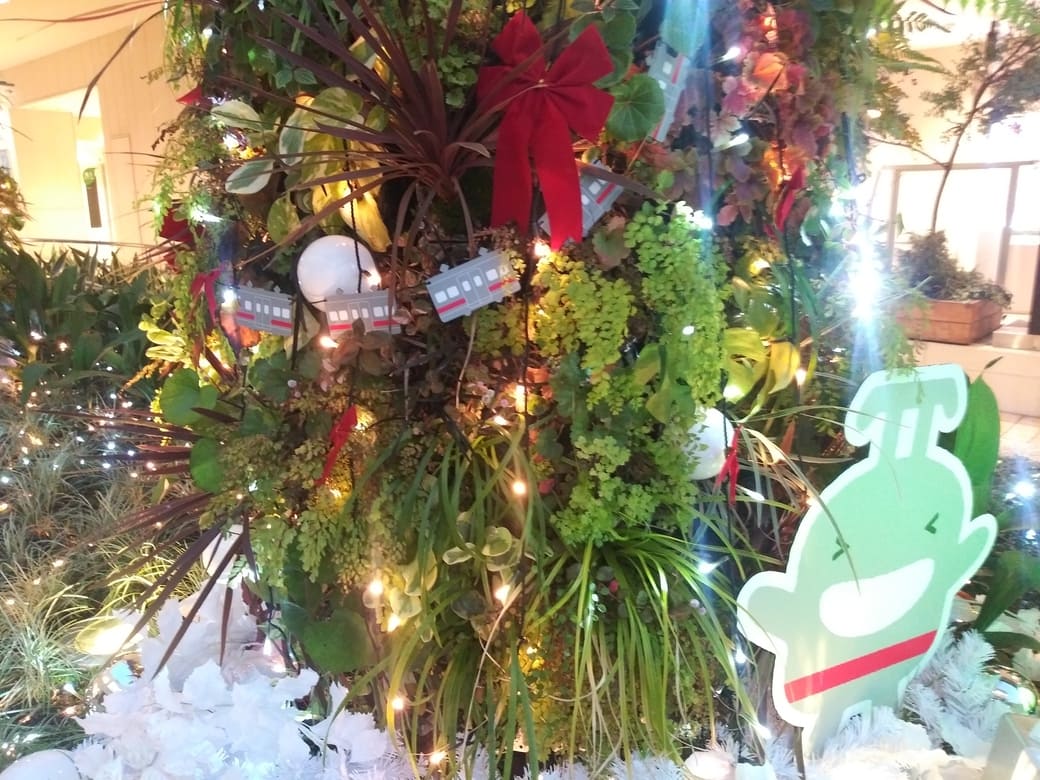 たまプラーザのクリスマスイルミネーション2025年_GATE PLAZA_交番側からカルディ方向への通路植え込みにあるのるるんのオブジェとライトアップされたディスプレイ　笑顔ののるるんの後ろには連射のオブジェが連なっている