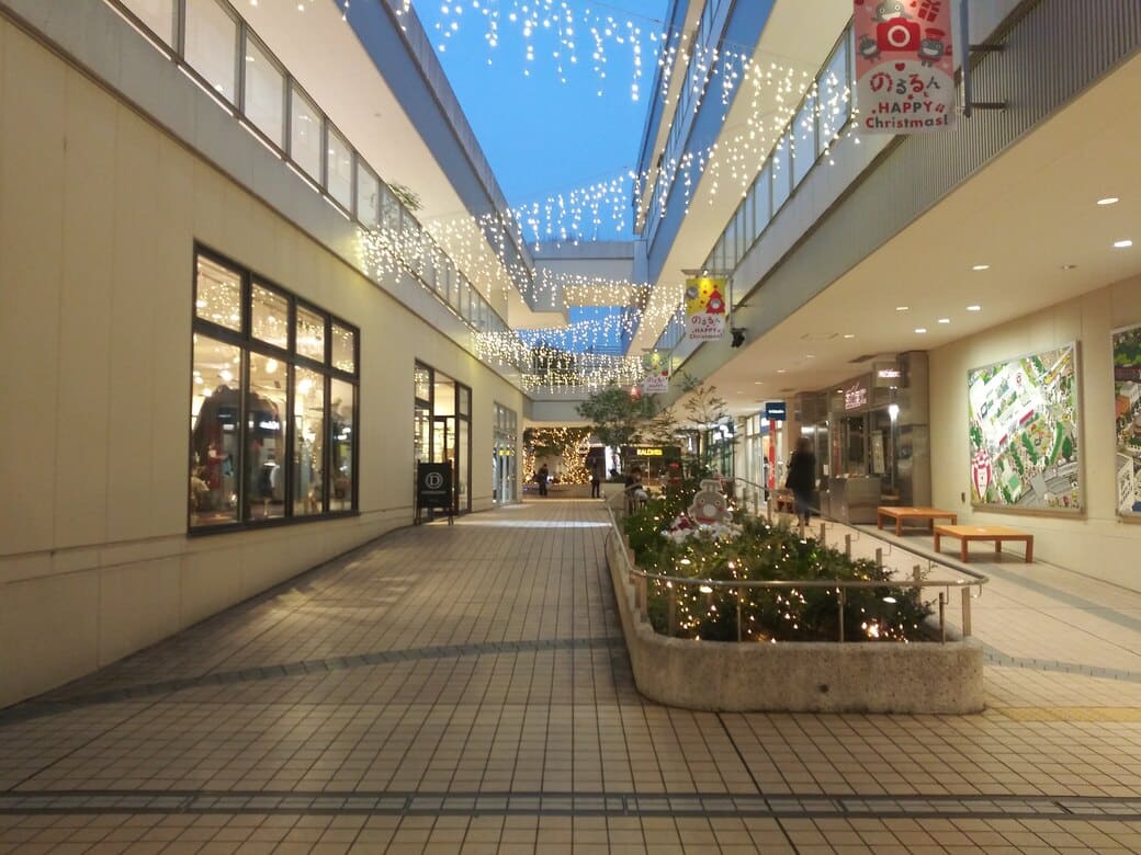 たまプラーザのクリスマスイルミネーション2025年_GATE PLAZA_交番側からカルディ方向への通路　中央の植え込みにあるのるるんのオブジェとライトアップされたディスプレイ