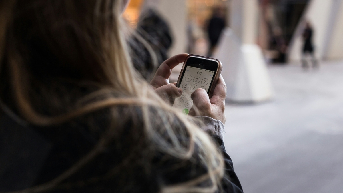 屋外でスマートフォンのダイヤル画面を表示し、両手を使って電話番号を入力している長い髪の女性の手元のアップ