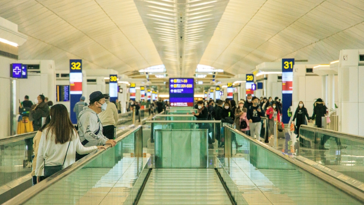 空港内の動く歩道を利用する旅行客たち。遠くまで続く通路と、搭乗ゲートを案内する青い看板