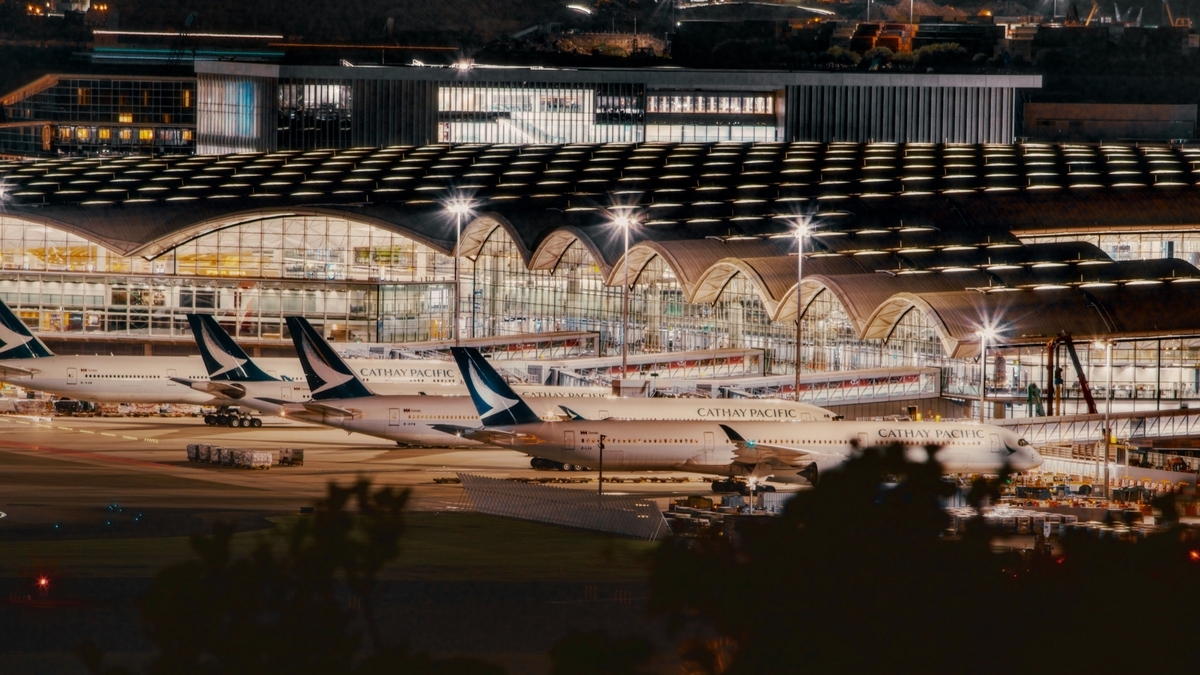 夜の香港国際空港。ライトアップされた波打つような屋根のターミナルを背景に、駐機場で出発を待つキャセイパシフィック航空の機体。
