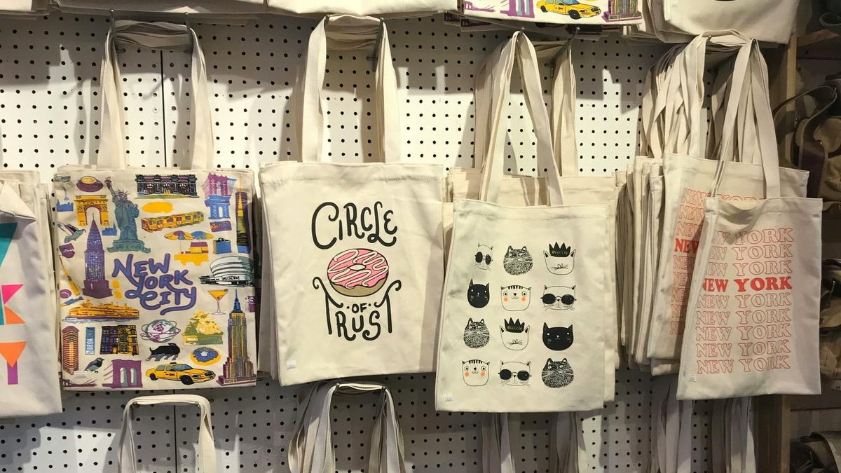 ニューヨークの名所やタクシーが描かれたトートバッグが、店内の白いパンチングボードに並んで吊るされている様子
