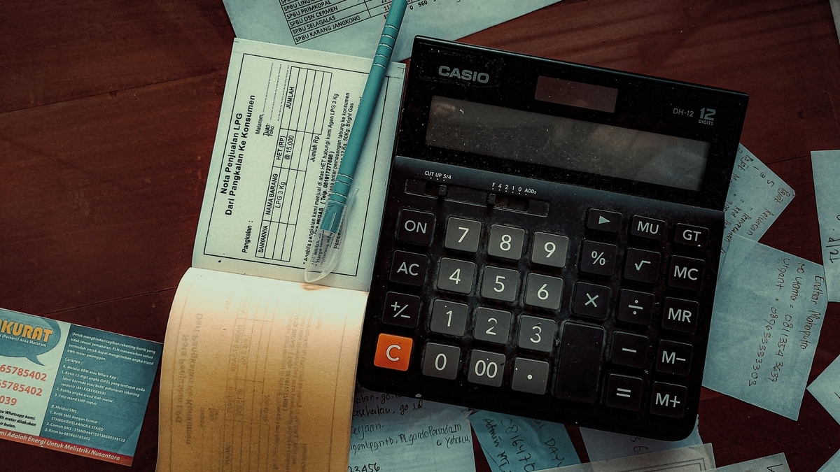 領収書やメモ書きが散らばったテーブルの上で、CASIO製の黒い卓上計算機と水色のペンが置かれている様子。
