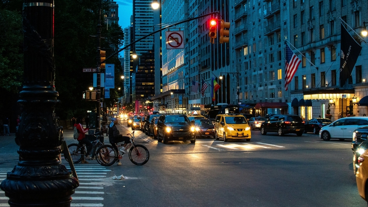 夕暮れ時のニューヨーク。ヘッドライトを点灯させた車や黄色いタクシーが行き交う交差点
