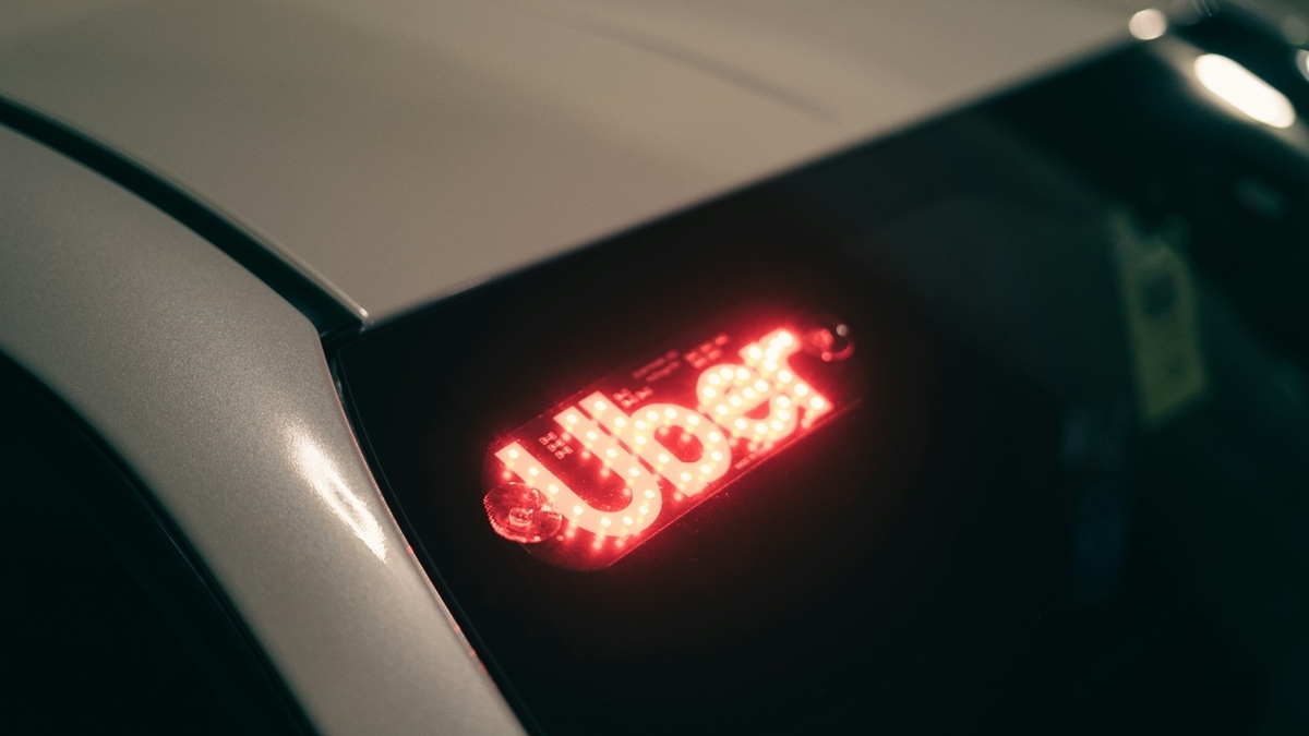 夜の暗がりに停車するシルバーの車のフロントガラスに、赤色に発光するUberのロゴサインが吸盤で固定されている様子。LEDの光が周囲をぼんやりと照らしている