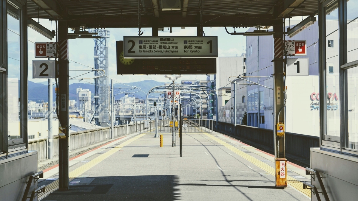 JR西日本の嵯峨野線が通る駅のホーム。頭上には「京都方面」や「亀岡・園部方面」と記された行き先案内板が掲げられています。線路の先には山々が見え、静かな駅の風景が広がっています