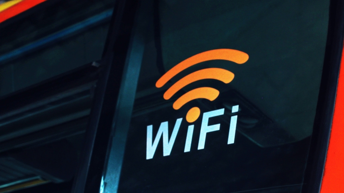 黒い窓ガラスのような表面に、オレンジ色の電波マークと白文字の「WiFi」というテキストがプリントされたステッカーが貼られており、公共の場での通信スポットを示している