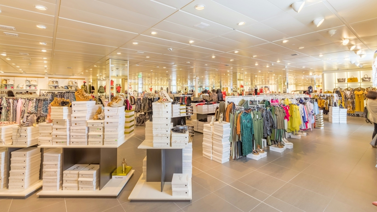 奥行きのある広々とした店内に、白い靴箱が積み上げられた什器と、色とりどりの洋服が並ぶハンガーラックが整然と配置されたアパレルショップの風景
