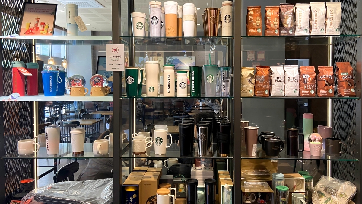 スターバックスの店内に設置されたガラス張りの棚に、色とりどりのタンブラーやマグカップ、コーヒー豆の袋が種類ごとに整然と並べられ、販売されている様子