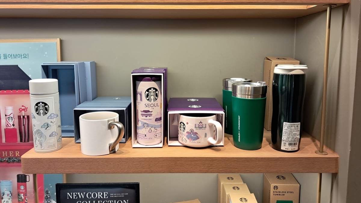 木製の棚に、スターバックスのロゴやソウルの街並みがデザインされた限定デザインのタンブラーやマグカップ、グリーンのステンレスボトルが箱入りで並んでいる陳列棚