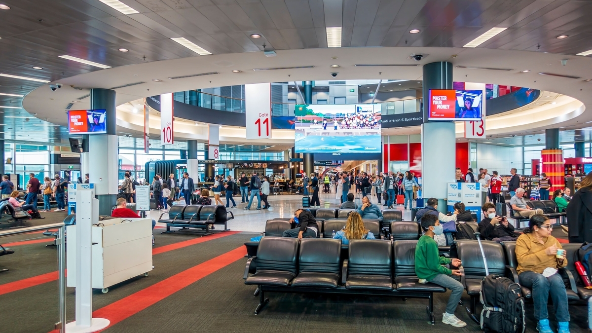 赤とグレーのカーペットが敷かれた空港の搭乗待合ロビーで、搭乗口11番付近の椅子に座り待機する乗客たち