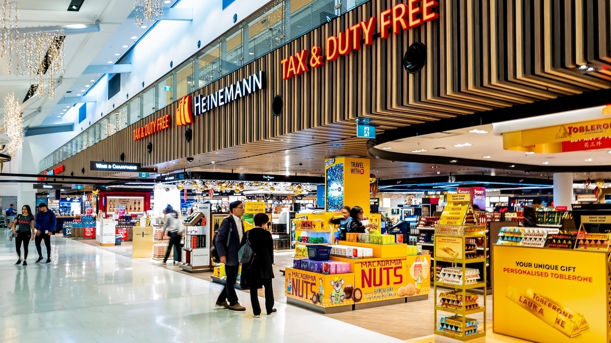 ハイネマンの免税店が並ぶ空港内の通路で、マカダミアナッツやトブラローネの黄色い看板が目を引く売場