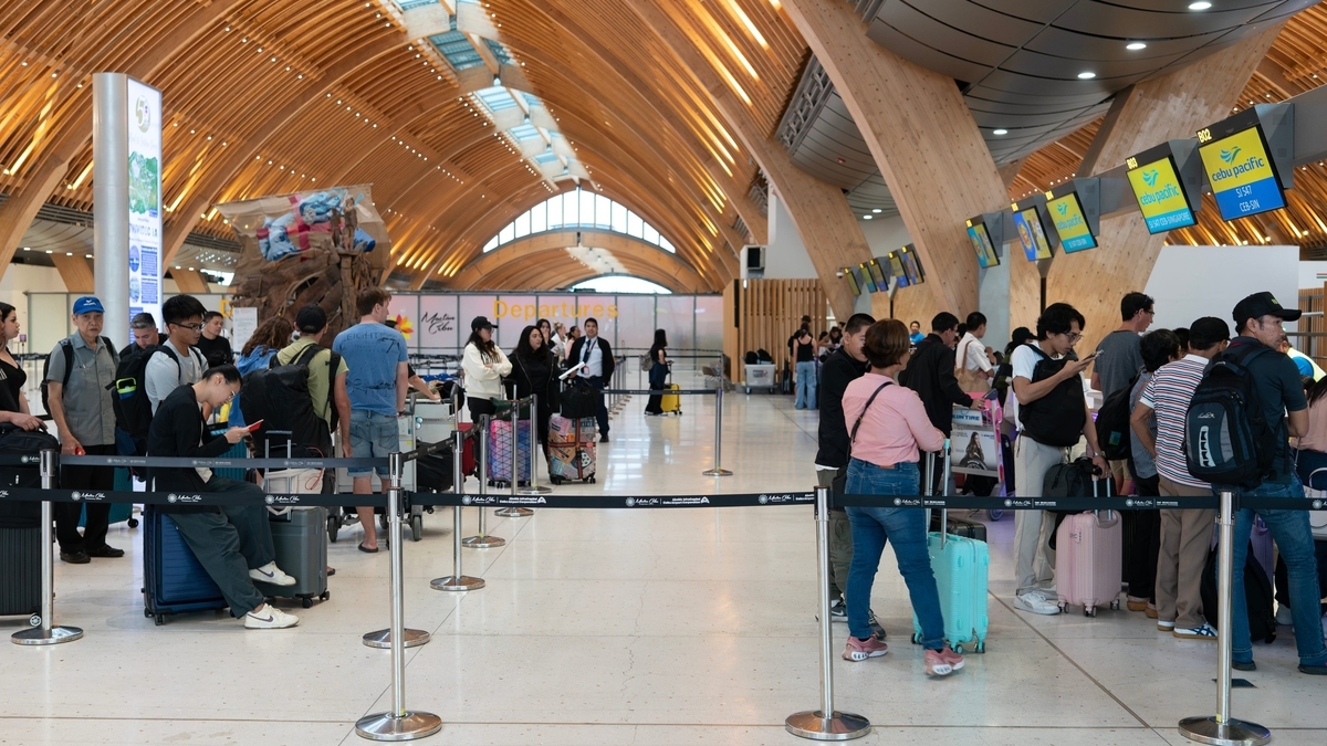 アーチ状の木製天井が特徴的な空港のチェックインカウンターで、スーツケースを持ち列に並んで順番を待つ多くの旅行者たち