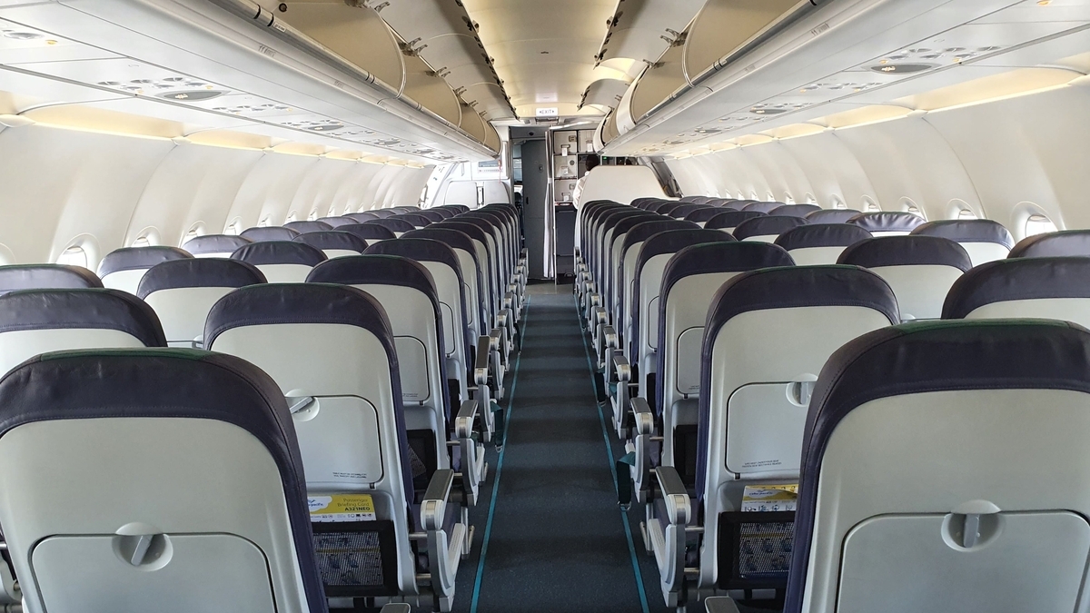 左右に3列ずつグレーの座席が並ぶ飛行機の機内通路と、上部の荷物収納棚が続く、乗客のいない静かな客室の様子