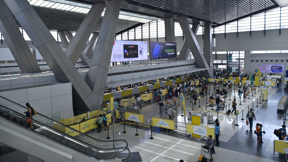 セブパシフィック航空の黄色いカウンターが並ぶ空港のチェックインロビー。大勢の旅行客がスーツケースを持って列を作り、順番を待っている様子を上階から見下ろした景観