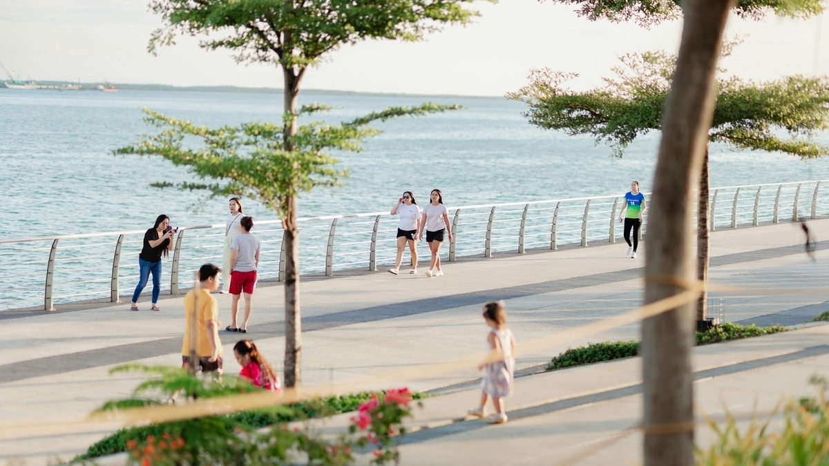 海沿いに続く白い手すりのある遊歩道を、半袖姿の人々が思い思いに散策している風景