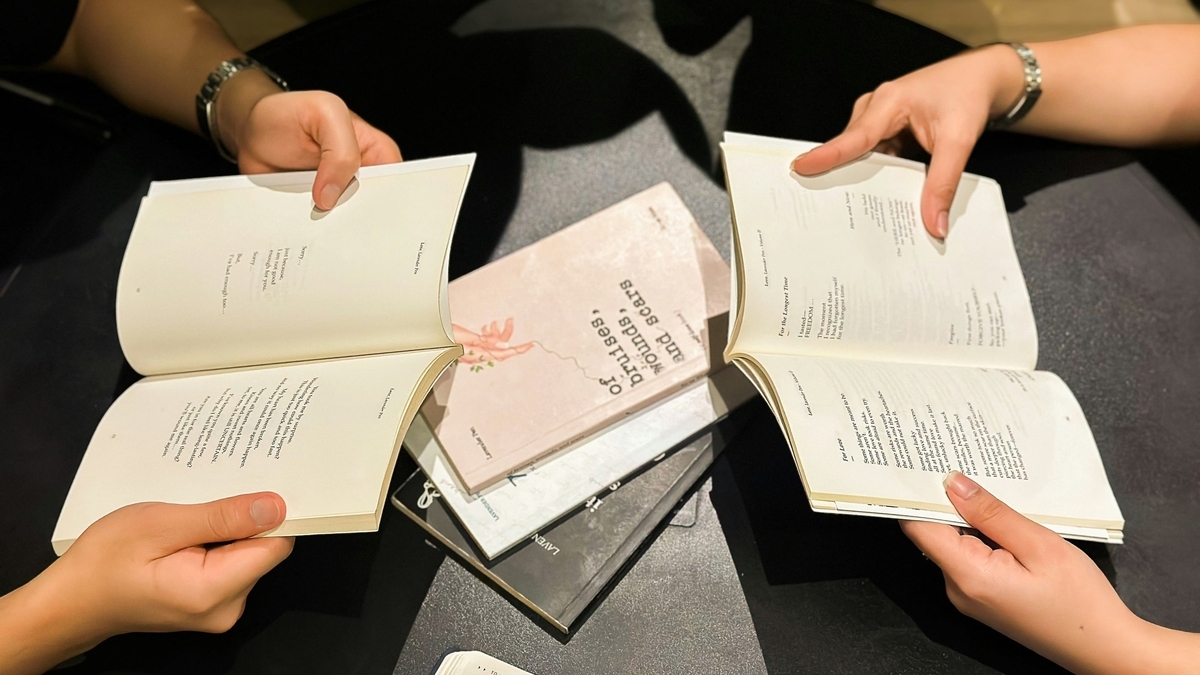 黒いテーブルの上で、数人がそれぞれ開いた本を手に持ち、詩のような文章を読んでいる様子