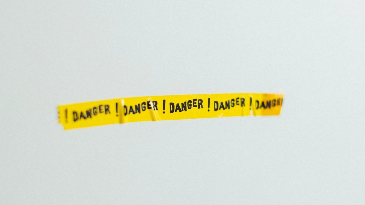 真っ白な背景の中央に、黒い文字で「DANGER」と繰り返し印字された黄色い粘着テープが水平に貼られている様子