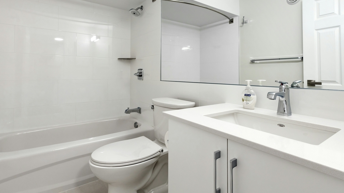 白を基調とした清潔感のあるバスルーム。手前に洗面台と鏡があり、奥にトイレとシャワー付きのバスタブが設置されている