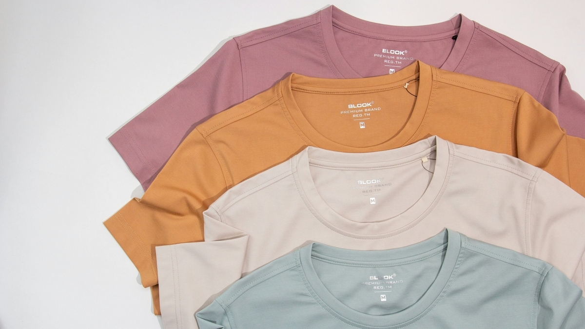 白地の背景に、くすんだピンク、オレンジ、ベージュ、ライトブルーの4色のクルーネックTシャツが、襟元を見せるように等間隔で重ねられた様子