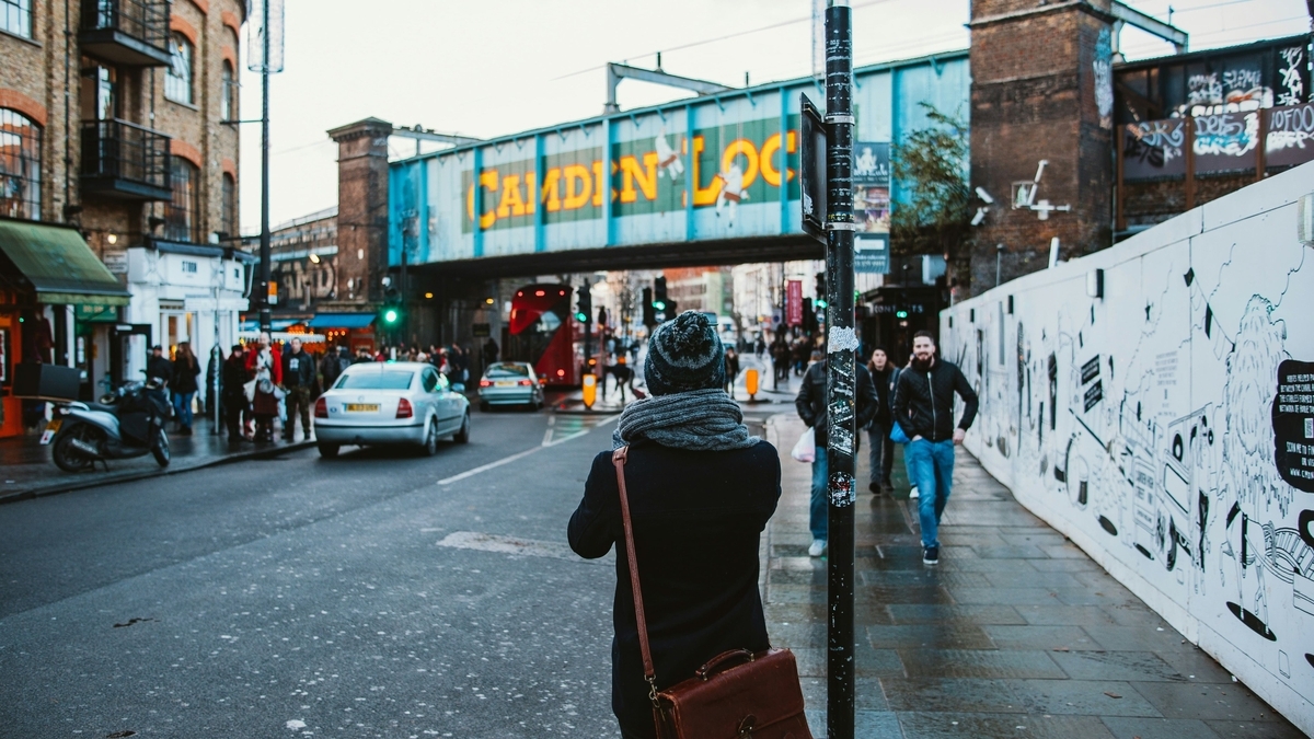 青い鉄橋に「CAMDEN LOCK」の黄色い文字が描かれた、カムデン・タウンの通りを歩く人々と街並み