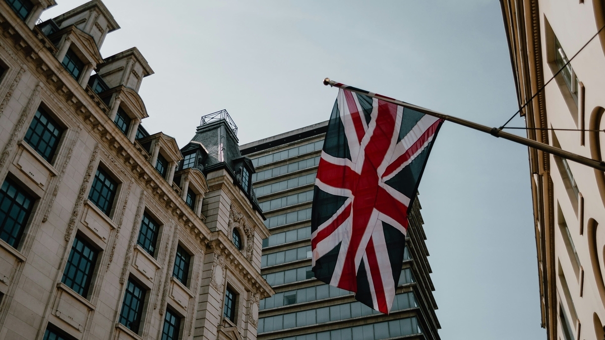 歴史的な石造りのビルと近代的なビルの間に掲げられた、風に揺れるイギリスの国旗（ユニオンジャック）