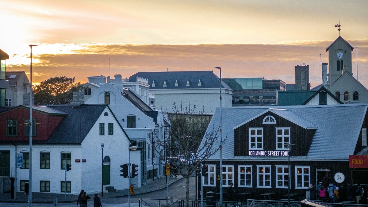 夕暮れ時の街並み。手前には「ICELANDIC STREET FOOD」の白い文字が光る黒い木造の建物があり、奥には教会のような尖塔が見えます。雲の隙間からオレンジ色の夕日が差し込み、空を淡く染めています