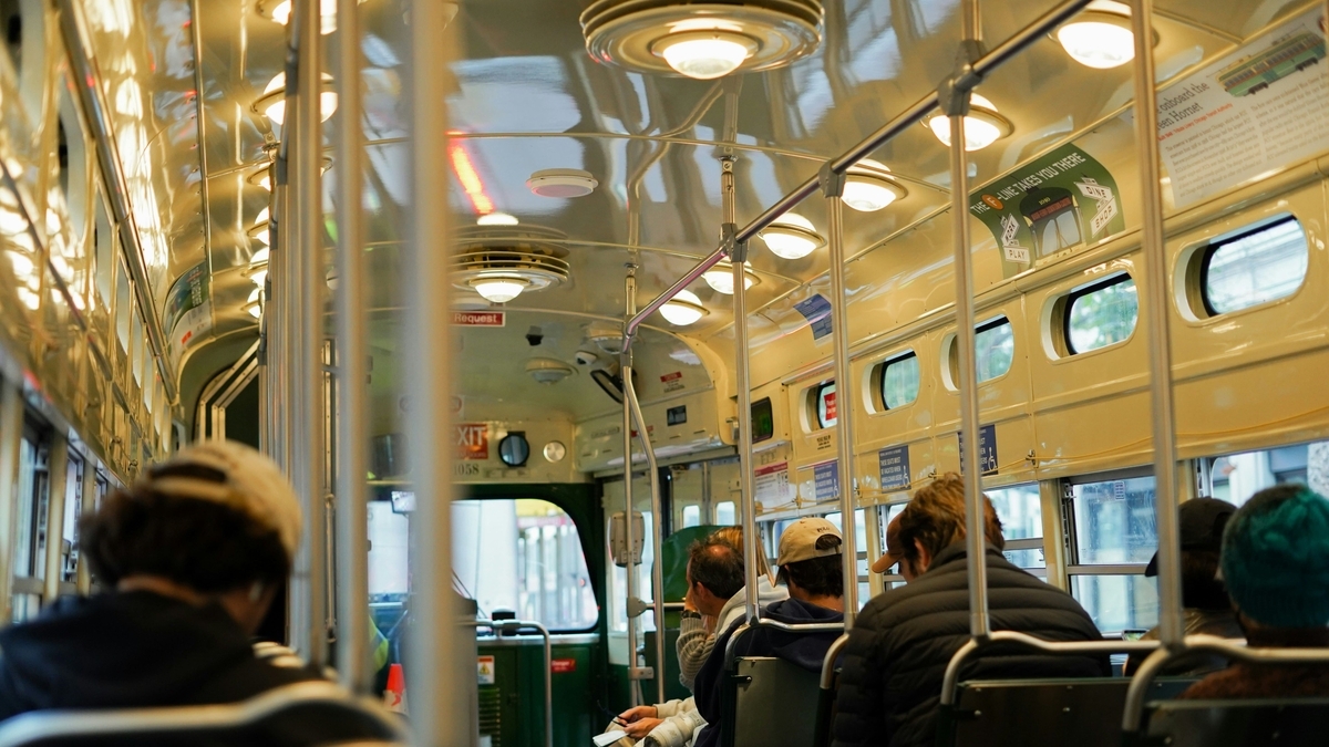 サンフランシスコのヴィンテージな路面電車の内観。レトロな照明が光る天井、金属製のポール、そして座席に座る乗客たちの姿が写っています