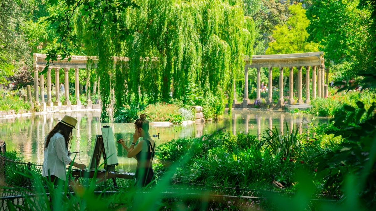 モンソー公園の池のほとりで、キャンバスに向かって絵を描く2人の女性。背景にはコリント式の柱が並ぶ半円形の回廊(ナウマキア)と、新緑の豊かな木々が写っています。