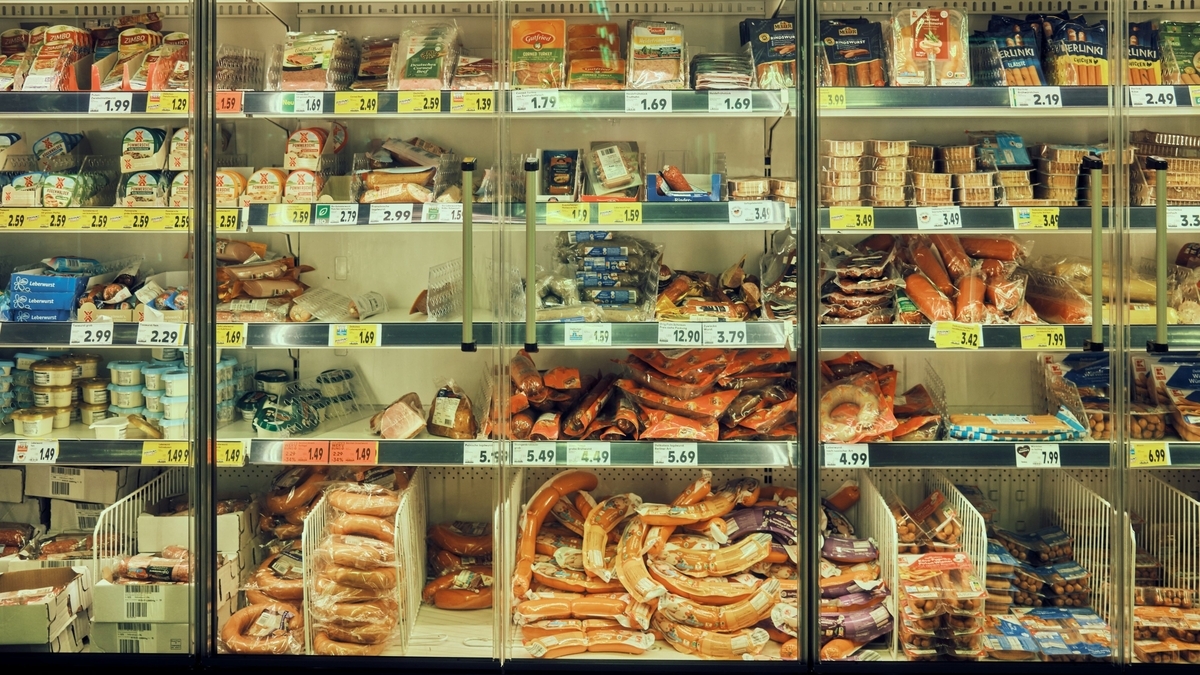 冷蔵ショーケースの棚に、値札とともにパッキングされた大量のハムやソーセージ、加工肉製品が整然と並んでいる様子