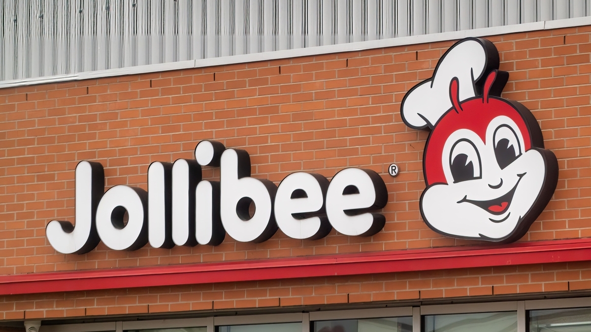 レンガ調の壁面に設置された、赤い蜂のキャラクターと白文字の「Jollibee」という看板ロゴのアップ